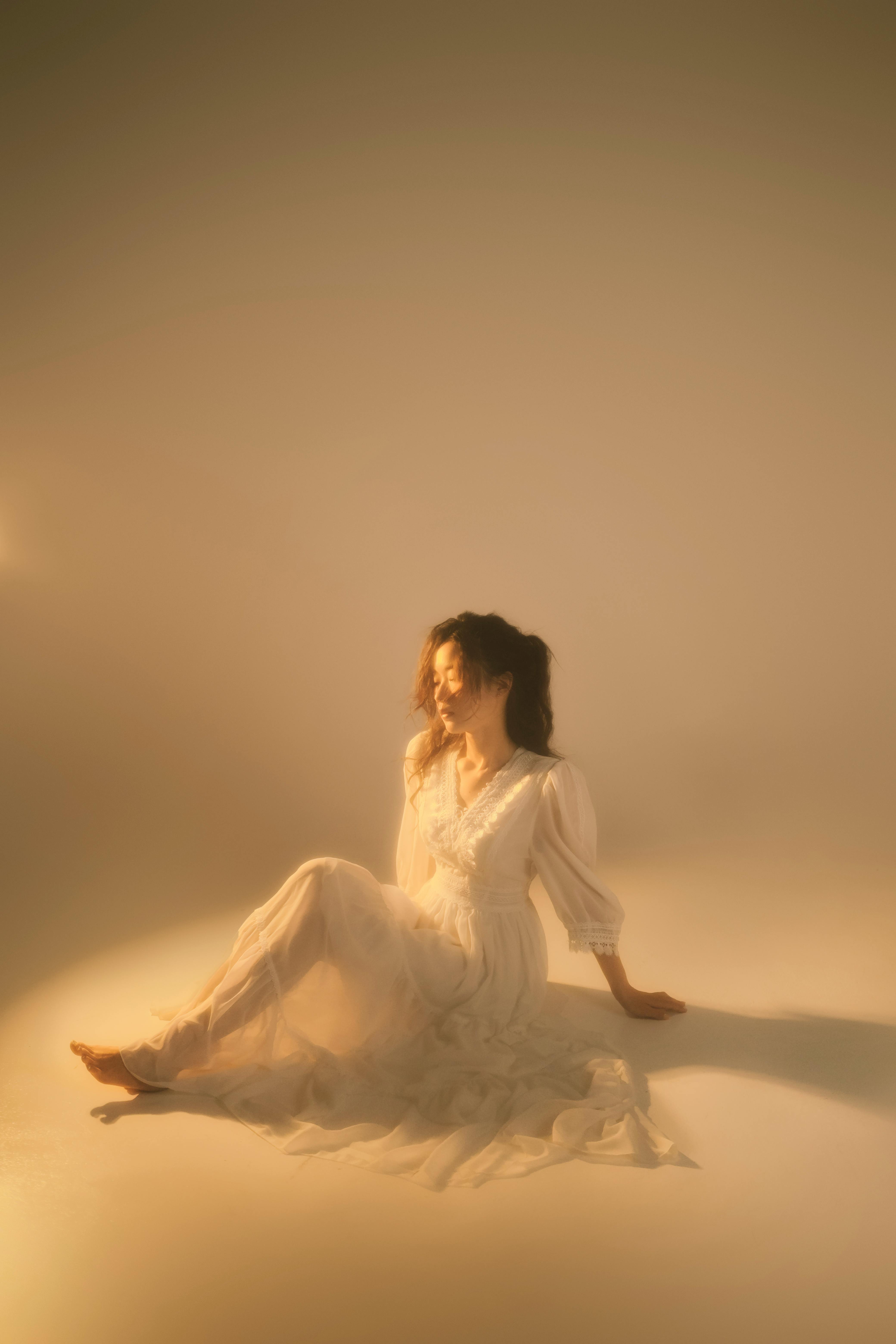 Soft-focus portrait of a woman in a white dress, sitting in a warm glow.